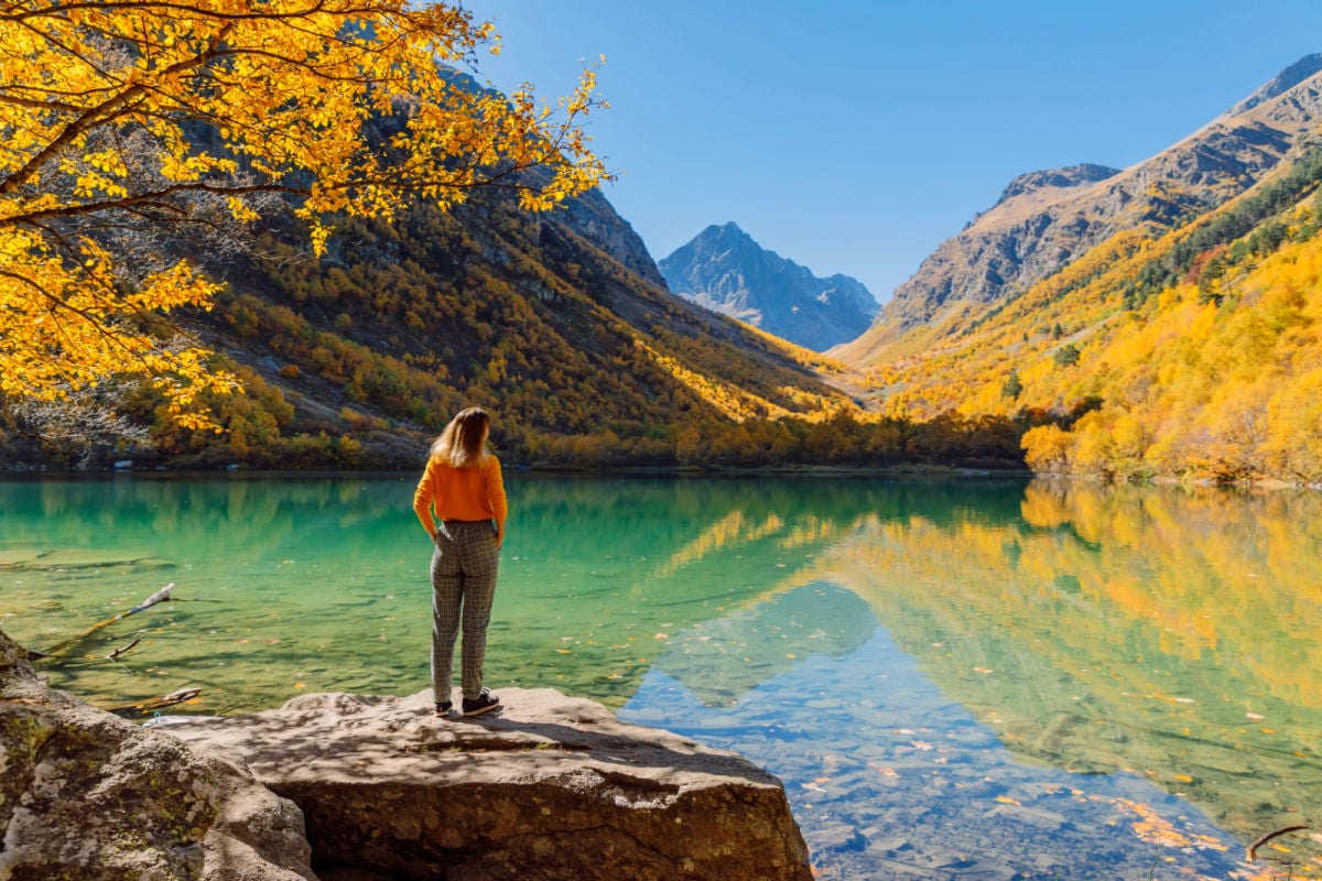 Portrait of hiker happy woman at lake in the autumnal mountains. Mountain lake and tourist