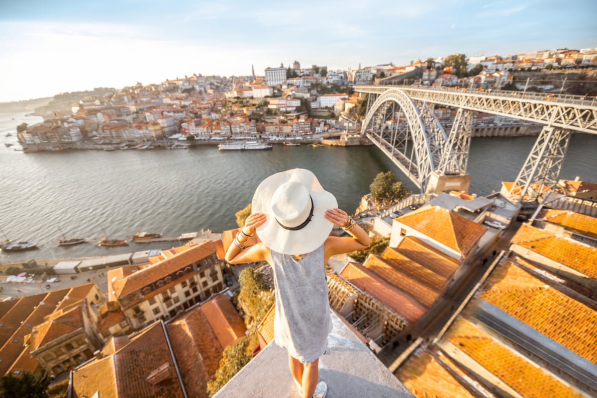 Young woman tourist enjoying beautiful landscape view on the old town with river and famous iron bridge during the sunset in Porto city, Portugal